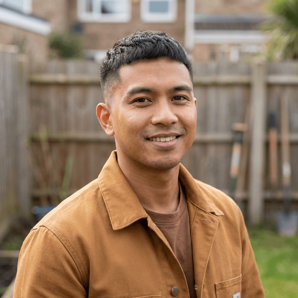 Smiling man with short dark hair wearing a brown canvas jacket in a backyard.