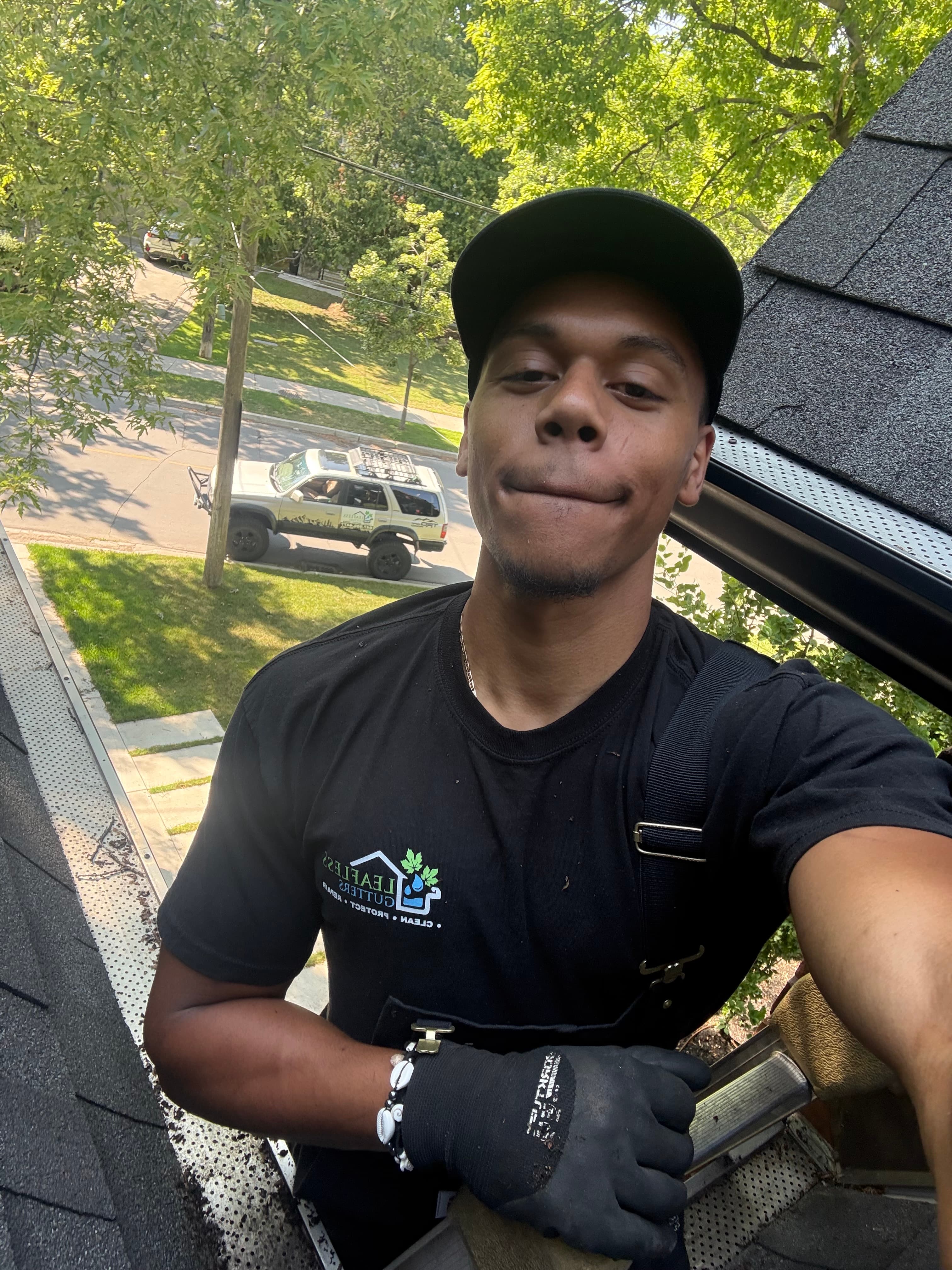 Man in a black Leafless Gutters shirt takes a selfie while working on a roof.